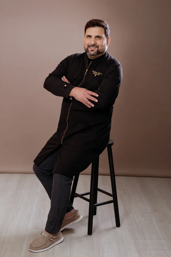 Verlano Alves seated on a stool in his studio jacket
