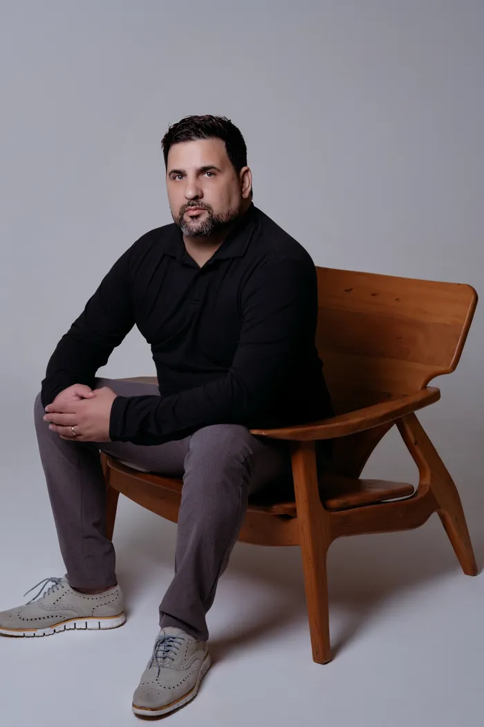 Verlano Alves seated in a wooden chair, dressed in black